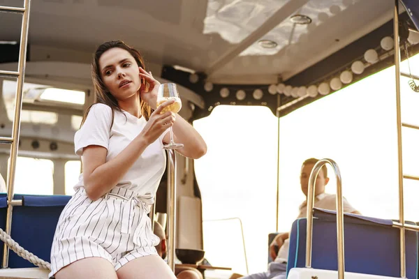 Νεαρή γυναίκα που κρατά ένα ποτήρι κρασί και κάθεται στο κατάστρωμα του ιστιοπλοϊκού σκάφους — Φωτογραφία Αρχείου