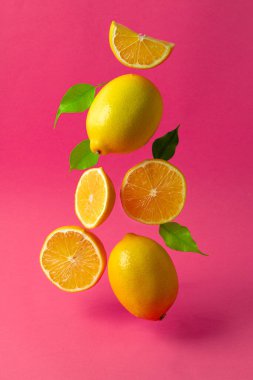 Parlak pembe arka planda havada asılı duran limonlar