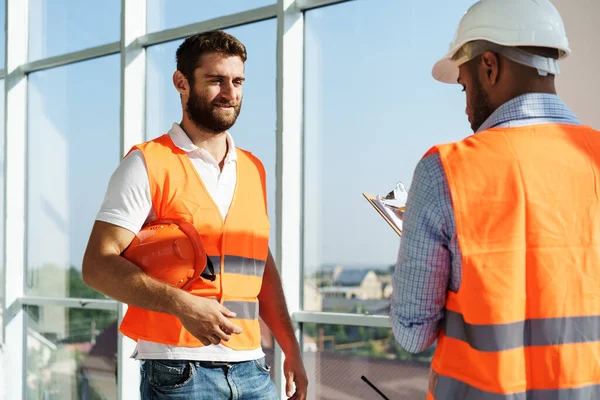 Två unga manliga ingenjörer i uniform och hatt arbetar på byggarbetsplatsen — Stockfoto