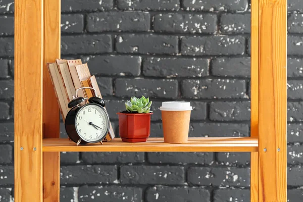Estante de madeira com livros e coisas contra parede de tijolo preto — Fotografia de Stock
