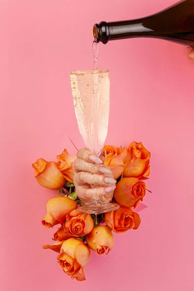 Vrouwelijke hand met manicure gieten champagne in een glas door een gat in een gescheurd papier versierd met rozen — Stockfoto