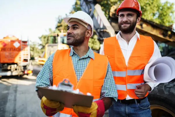 Två män ingenjörer diskuterar sitt arbete stående mot byggmaskiner — Stockfoto