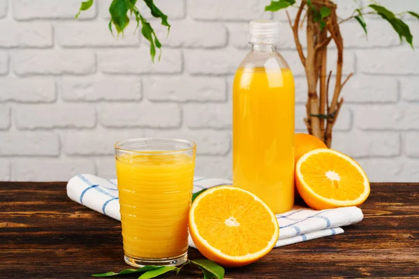 Бутылка свежего апельсинового сока на деревянном столе на фоне стены из белого кирпича — стоковое фото