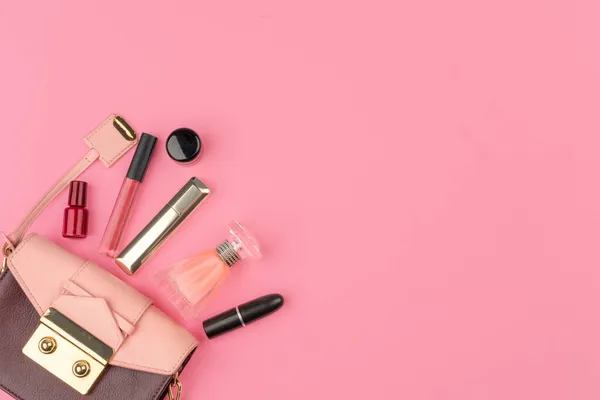 Piccola borsa femminile piena di prodotti cosmetici su sfondo rosa brillante — Foto Stock