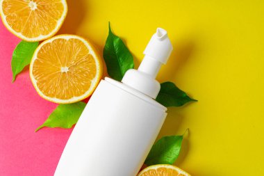 Parlak pembe arka planda dilimlenmiş narenciye meyveli kozmetik şişesi.