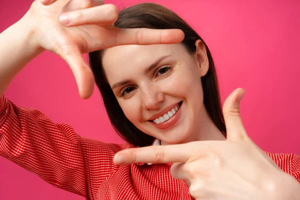 Sorridente giovane donna mostrando cornice con le dita sullo sfondo rosa. — Foto Stock