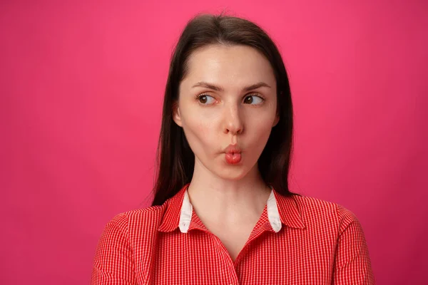 Retrato de uma jovem bonita chupado em suas bochechas contra fundo rosa — Fotografia de Stock
