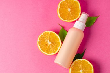 Parlak pembe arka planda dilimlenmiş narenciye meyveli kozmetik şişesi.