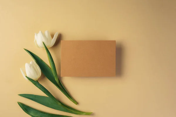 Cartão de papel artesanal cercado por tulipas frescas em fundo bege — Fotografia de Stock
