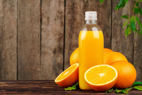 Botella de jugo de naranja con naranjas sobre mesa de madera — Foto de Stock