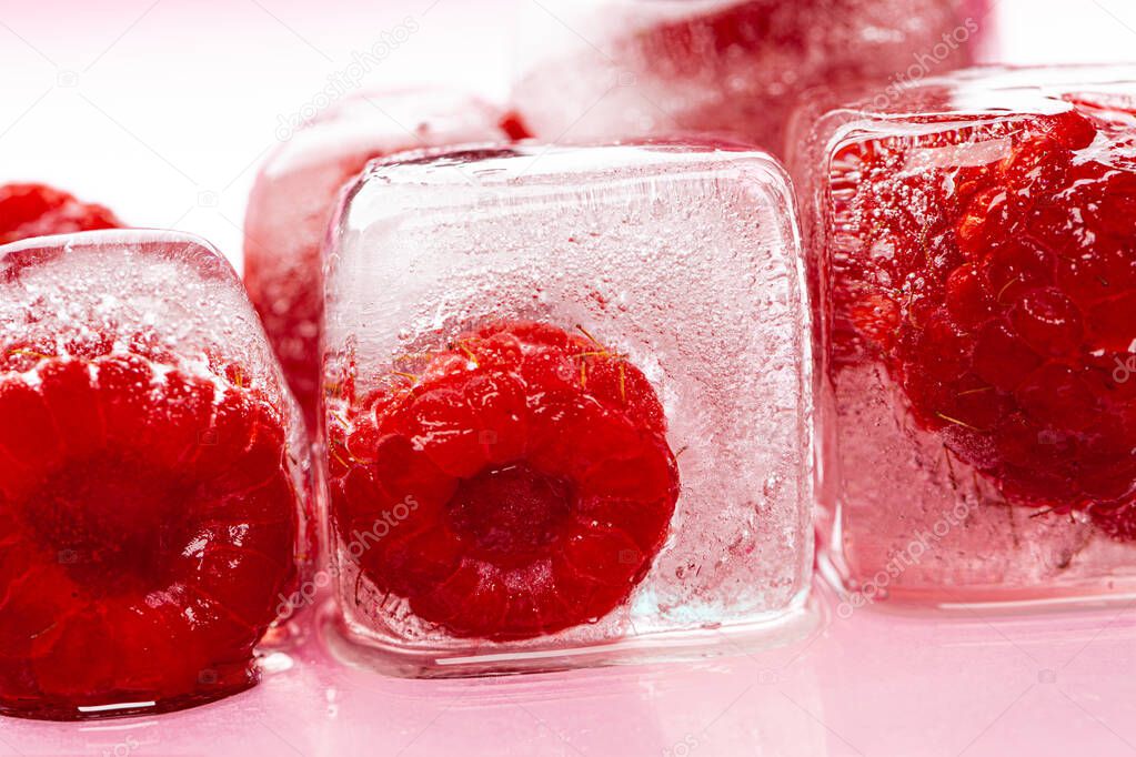 Raspberry ice cubes on pink glossy background