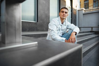 Sokakta tek başına merdivenlerde oturan sıradan bir genç.