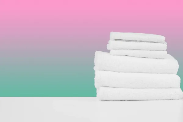 Stacked clean towels on white table against color background — Stock Photo, Image