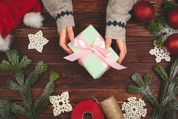 Manos en suéter sosteniendo un regalo en mesa de madera con decoraciones navideñas —  Fotos de Stock