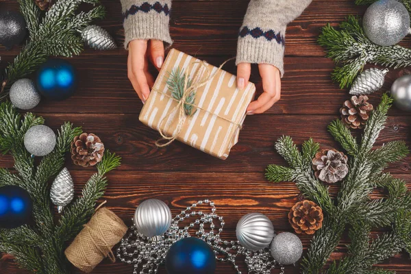 Dekorowany prezent ze wstążką otoczony świątecznymi dekoracjami na drewnianym stole — Zdjęcie stockowe