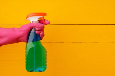 Sarı ahşap arka planda ev yapımı deterjan spreyi tutan eldiven.