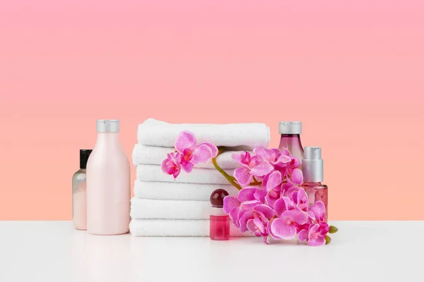Stack of white towels and bottles of skincare on white table — Stock Photo, Image