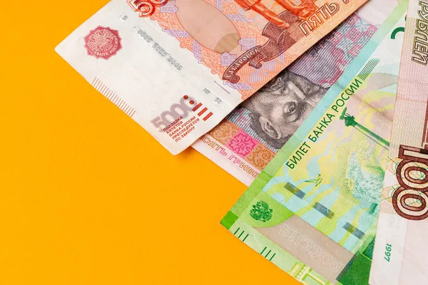 Billetes de rublos rusos y grivna ucraniana sobre fondo amarillo de cerca — Foto de Stock