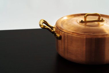 Siyah bir masada paslanmaz, parlak bakır tencere.