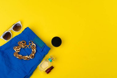 Parlak sarı arka planda aksesuarları olan şık bir kadın kıyafeti.