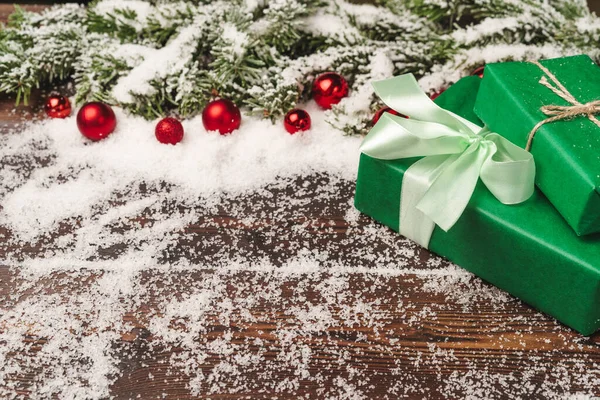 Подарунки на дерев'яному тлі з гілками ялинки та червоними вафлями, посипані снігом — стокове фото