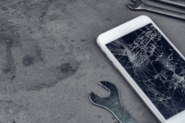 Gri arkaplanda tamir araçları ile çökmüş akıllı telefon