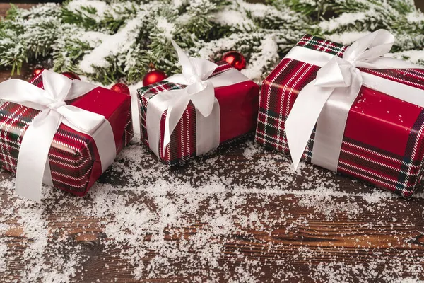 Подарунки на дерев'яному тлі з гілками ялинки та червоними вафлями, посипані снігом — стокове фото