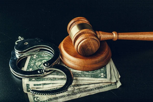 Bribe concept. Dollar banknotes, handcuffs and gavel on dark black table — Stock Photo, Image