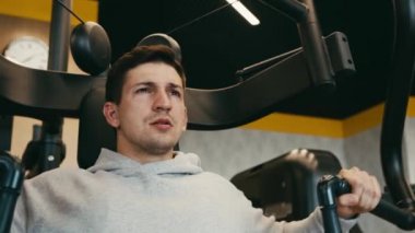 Gri kapüşonlu genç adam spor salonunda kollarını çalıştırıyor.