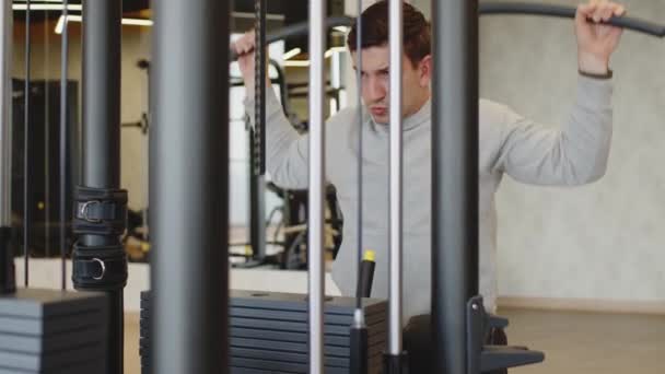 Junger Mann in grauem Kapuzenpullover trainiert Arme in Turnhalle — Stockvideo