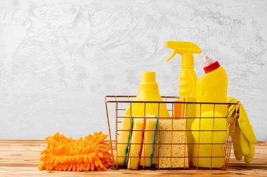 Temizlik aletleri ve kimyasallar sepetin içinde ahşap masa üzerinde gri arka planda