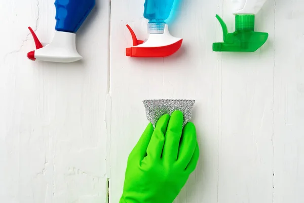 Hand in glove with cleaning supplies above white wooden background — Stock Photo, Image