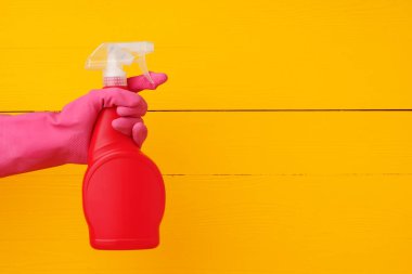 Sarı ahşap arka planda ev yapımı deterjan spreyi tutan eldiven.
