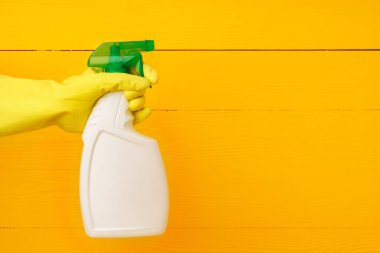 Sarı ahşap arka planda ev yapımı deterjan spreyi tutan eldiven.