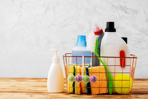 Herramientas de limpieza y productos químicos en cesta sobre mesa de madera sobre fondo gris — Foto de Stock