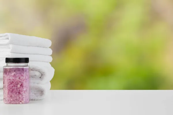 Bath salt bottle and towels against blurred background — Stock Photo, Image