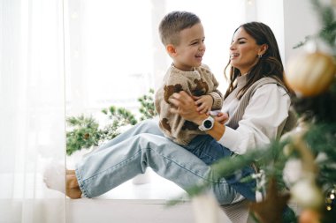 Mutlu anne ve oğlu Noel ağacının yanındaki pencere eşiğinde oturuyor.