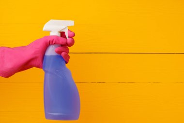 Sarı ahşap arka planda ev yapımı deterjan spreyi tutan eldiven.