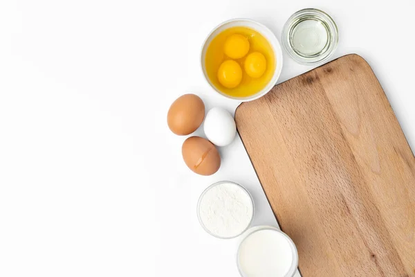 Фон для выпечки с сырыми яйцами и деревянной доской на белом — стоковое фото
