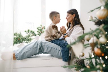 Mutlu anne ve oğlu Noel ağacının yanındaki pencere eşiğinde oturuyor.