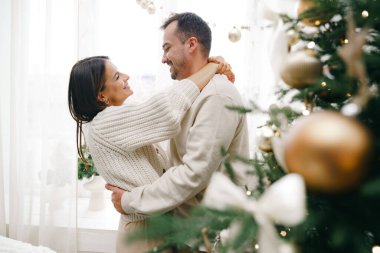 Genç çift evde Noel ağacının yanında sarılıyor.