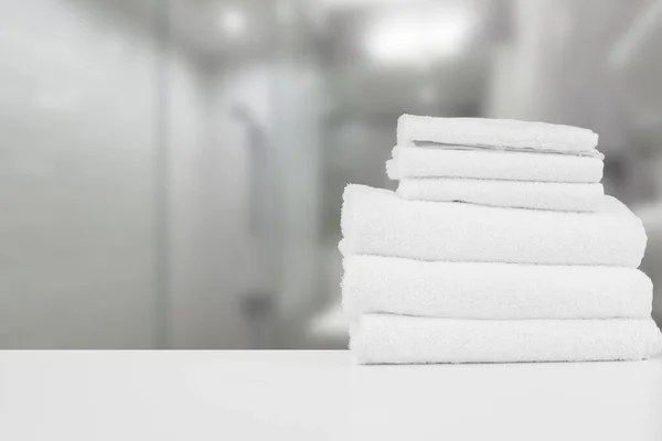 Staplade vita spa handdukar på bordet mot suddig bakgrund — Stockfoto