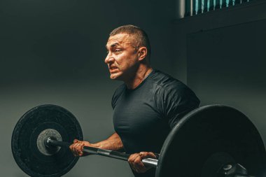 Spor kıyafetli kaslı adam spor salonunda halter kaldırıyor.