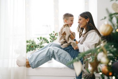 Mutlu anne ve oğlu Noel ağacının yanındaki pencere eşiğinde oturuyor.