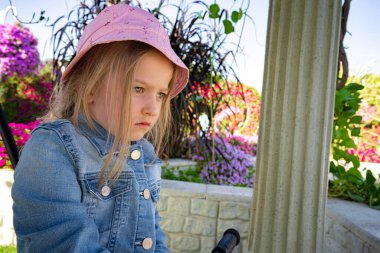 Pembe şapkalı üzgün küçük kız parkta oturuyor.