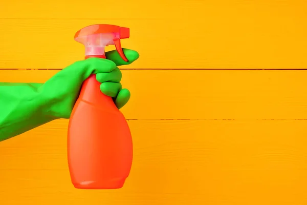 Hand in glove holding household detergent spray against yellow wooden background — Stock Photo, Image