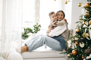 Mutlu anne ve oğlu Noel ağacının yanındaki pencere eşiğinde oturuyor.