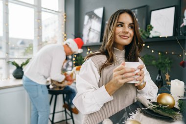 Çekici genç kadın Noel 'de mutfakta çay içiyor.