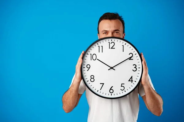 Hombre joven guapo en camiseta blanca posando con reloj sobre fondo azul — Foto de Stock