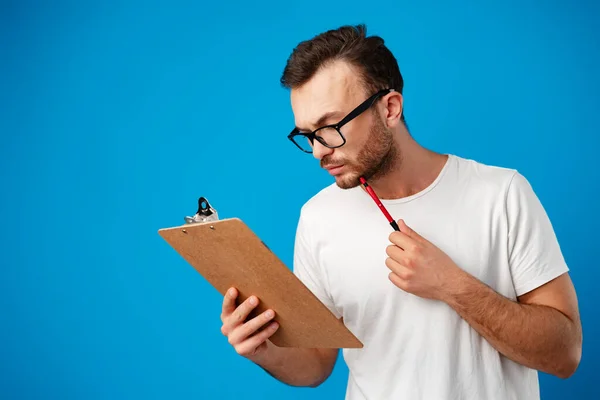 Portret van een jongeman die notities maakt op het klembord tegen een blauwe achtergrond — Stockfoto